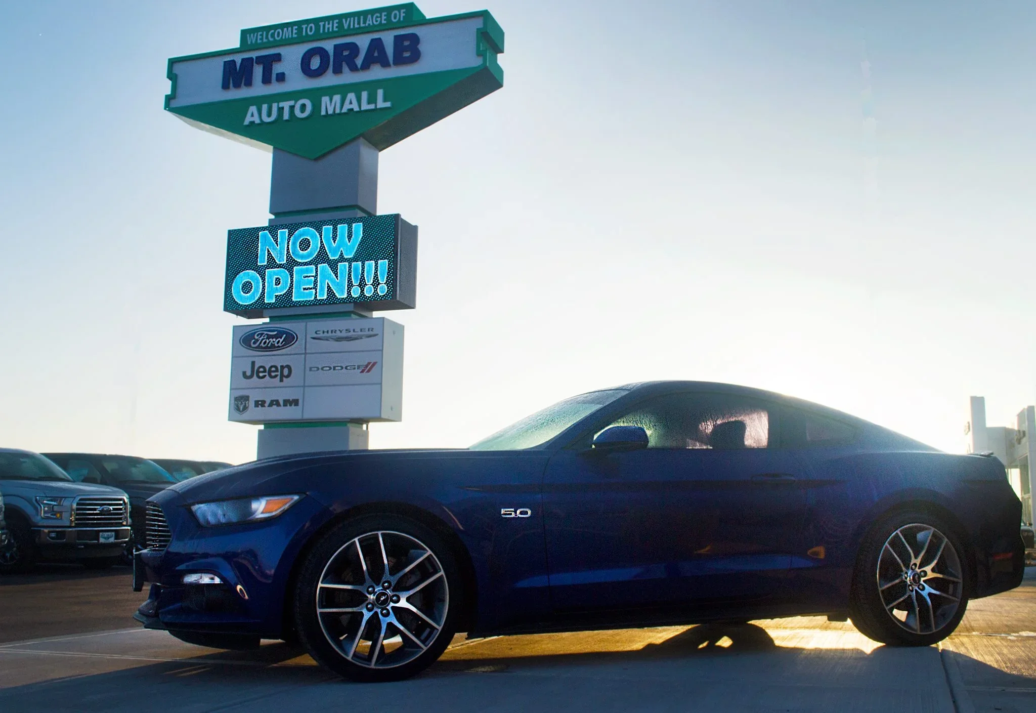 Blue Ford Mustang parked at Mt. Orab Auto Mall dealership sign reading “Now Open.”